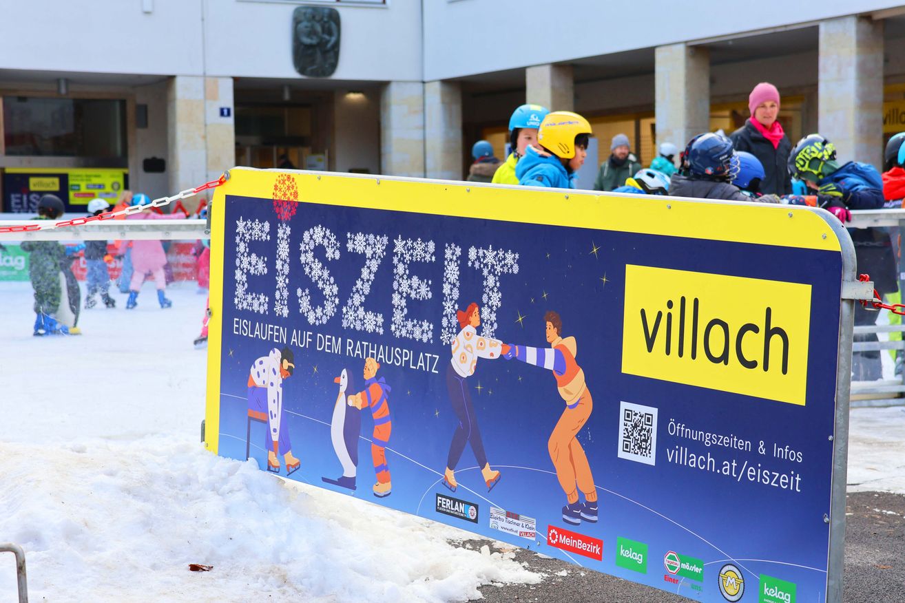 Ein buntes Schild, das Eislaufen auf dem Rathausplatz bewirbt, mit einer Illustration von Menschen beim Eislaufen und einem QR-Code. Es wird in einem verschneiten Bereich mit Menschen in Helmen angezeigt.