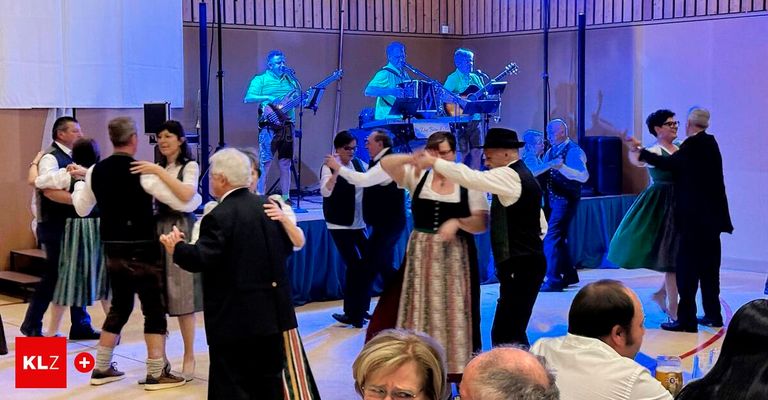 A group of people dance on stage while a band plays in the background. The dancers are dressed in traditional attire, and the musicians are playing various instruments.