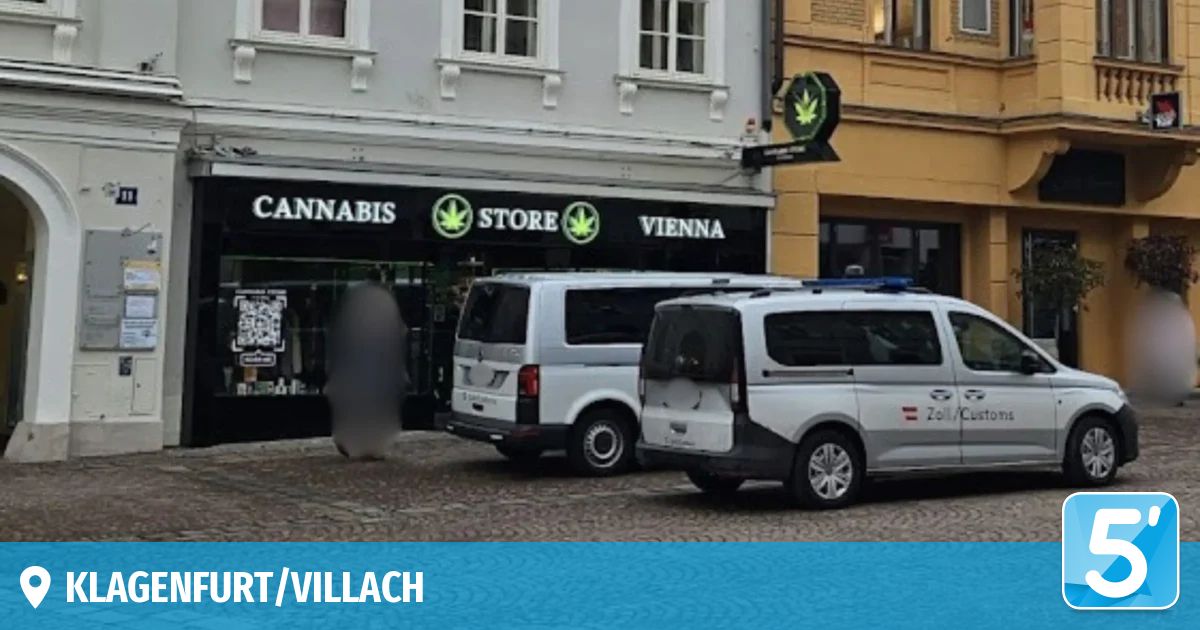 Zwei Polizeifahrzeuge sind vor einem Gebäude geparkt, an dem ein Schild mit der Aufschrift 'Cannabis Store Vienna' angebracht ist. Die Fahrzeuge haben Polizeikennzeichen und sind auf einer Kopfsteinpflasterstraße geparkt.