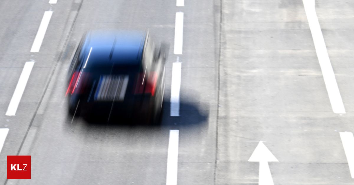 Ein dunkelblaues Fahrzeug fährt auf einer verschwommenen Straße mit weißen Markierungen und Pfeilen. Das Bild ist unscharf.