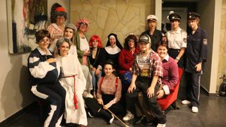 Eine Gruppe von Menschen in verschiedenen Kostümen posiert für ein Foto. Dazu gehören eine Nonne, ein Matrose, ein Soldat und einige andere.