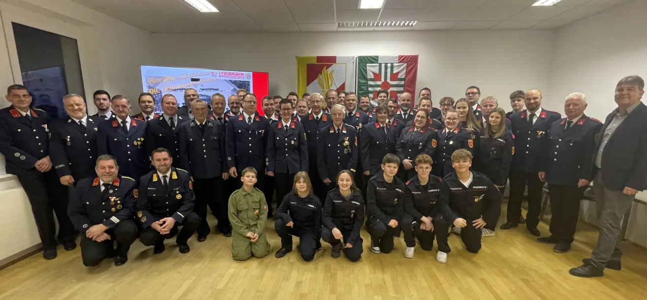 Eine Gruppe von Feuerwehrleuten und Auszubildenden posiert für ein Foto mit einigen Erwachsenen und Kindern vor einer Wand mit Bannern.
