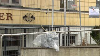 Ein Gebäude mit einem Schild, 'Rathausbrauerei', hat einen Metallzaun und eine abgedeckte Antenne. Ein weißes Netz ist auf einer Betonbarriere platziert.