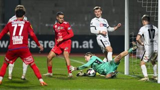 Fußballspieler in roten und weißen Trikots auf einem Feld; ein Spieler fällt, während ein anderer zusieht.