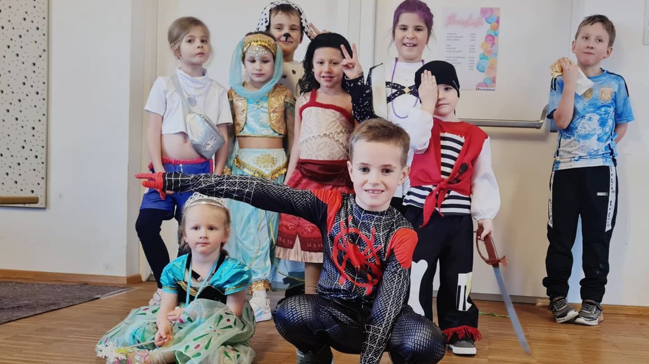 Several children in various costumes are posing for a photo, including a girl in a Spider-Man costume, a pirate, and a princess.
