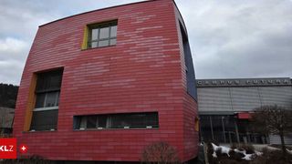 Ein modernes Gebäude mit roter Ziegelfassade und drei Fenstern. Es hat eine gebogene Fassade. Ein Schild sagt Campus.