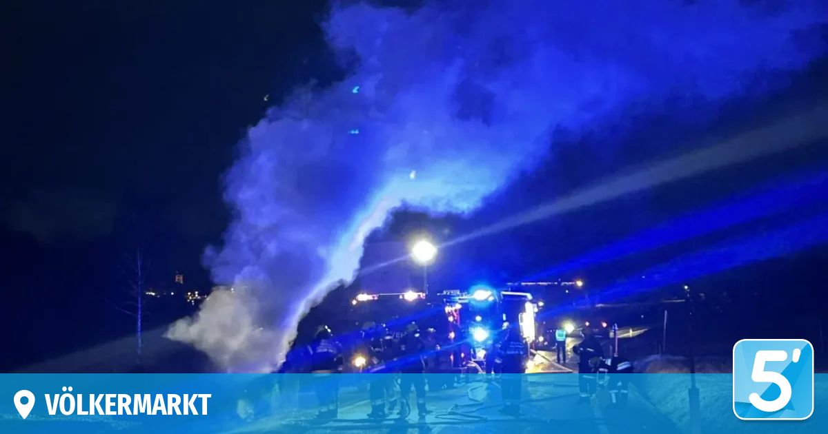 Bei Nacht füllt eine große blaue Rauchwolke den Himmel, mit geparkten Einsatzfahrzeugen in der Nähe und blinkenden blauen Lichtern, die die Szene beleuchten.