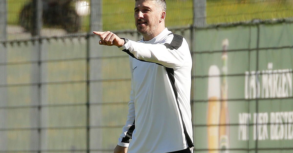 Ein Mann in einem weißen und schwarzen Langarmshirt zeigt mit dem Finger nach draußen auf etwas.