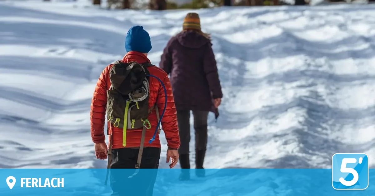 Zwei Personen gehen im Schnee, eine mit Rucksack und blauer Mütze, die andere in einem braunen Mantel und Mütze.