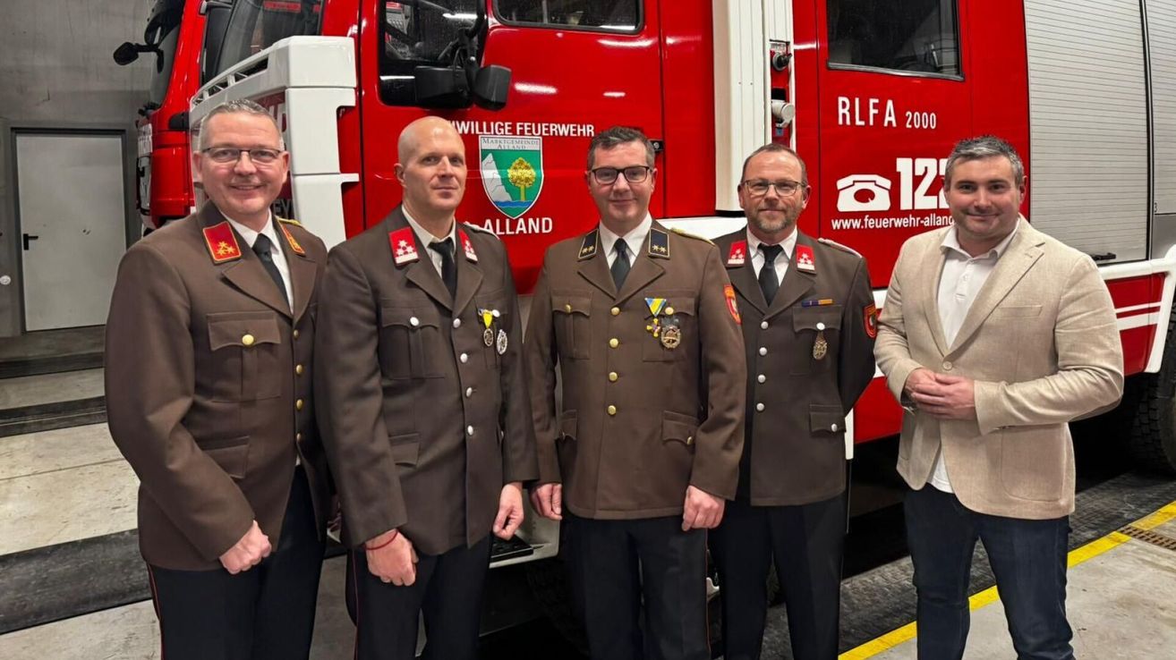 Five men in military uniforms are standing in front of a red fire truck, likely in a ceremonial setting.