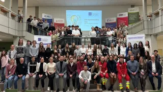 Eine Gruppe von Studenten und Pädagogen posiert für ein Foto auf einer Treppe, mit einem Banner für 'Entrepreneurship Day' und einem Glühbirnendesign im Hintergrund.