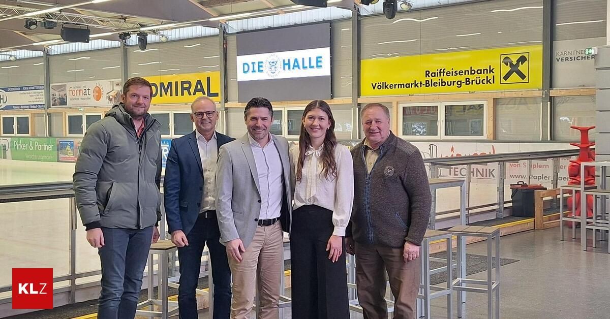 Fünf Personen stehen gemeinsam in einer Halle. Der Mann links trägt einen grauen Mantel. Die Frau in der Mitte trägt eine weiße Bluse. Hinter ihnen steht ein gelbes Schild mit der Aufschrift 'Die Halle'.