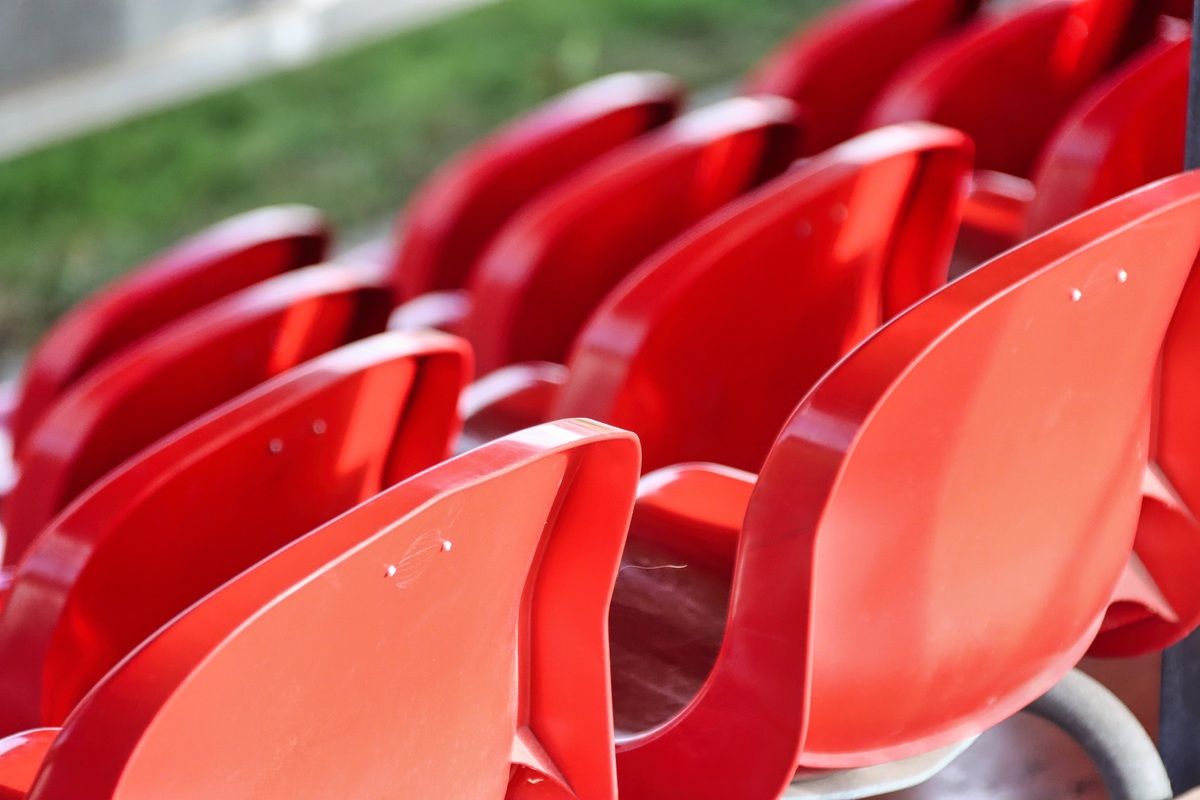 Close-up of red stadium seats arranged in rows, with a blurred green field in the background.
