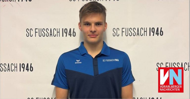 A man stands in front of a wall with the text 'SC 1946' and 'Fussbach 1946'. He wears a blue and black shirt with 'SC Fussbach 1946' and a logo on the left side. He has short hair and is smiling.