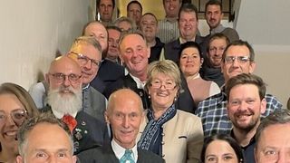 A group of people, some wearing glasses and formal attire, are standing in a line and posing for a photo.