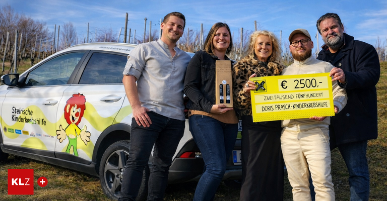 Four people stand in front of a car with a cheerful clown painted on it. Two women and a man are smiling. The women hold a box and a yellow board with the text Zweitausend Funfhundert.