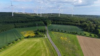 Aerial view of a rural landscape with several wind turbines on a hill and a road leading through green fields.