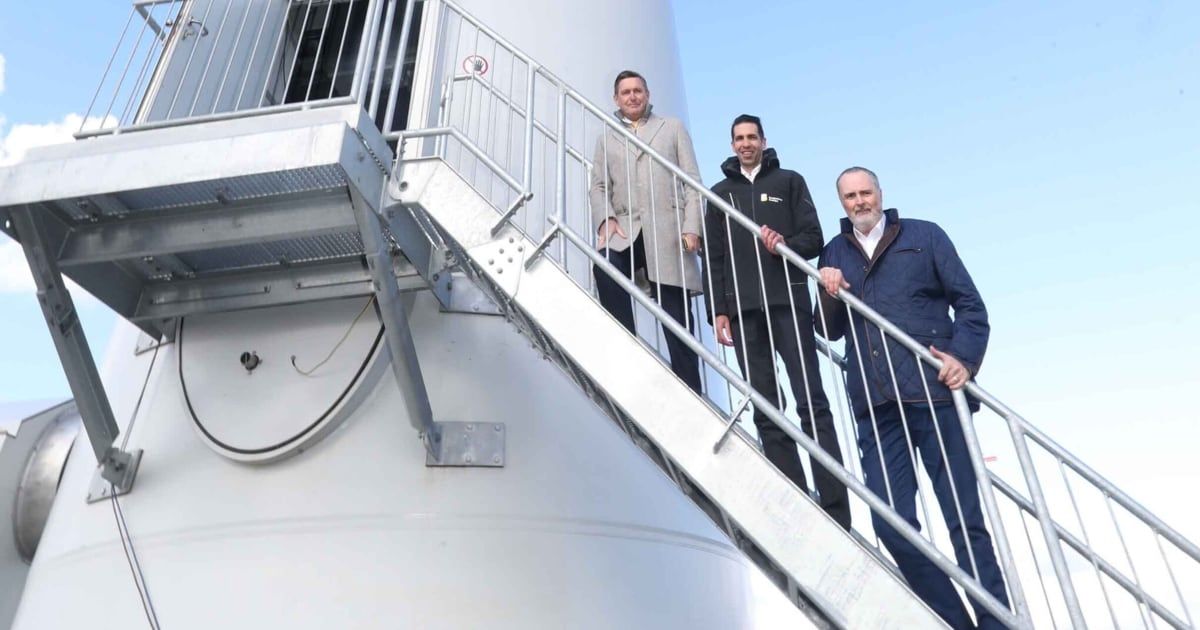 Three men are standing on a staircase leading to the top of a wind turbine. They are smiling and seem to be posing for a photo.