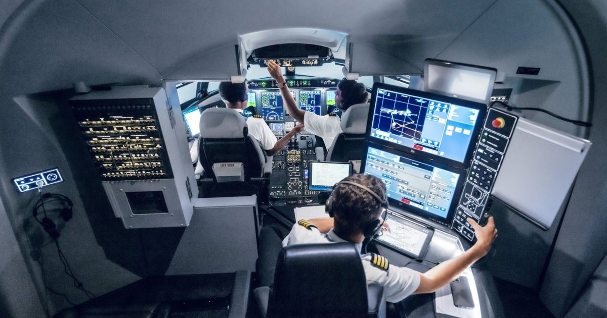The cockpit of a modern aircraft with three pilots. Two pilots sit at the controls, one in the middle points to the screen. The front pilot has headphones on.