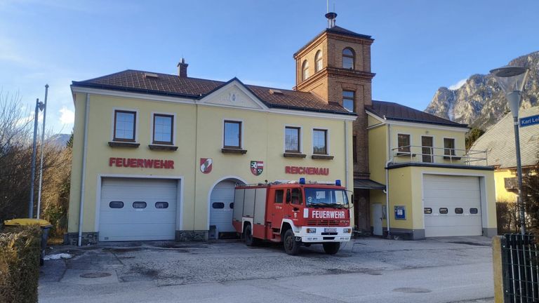 A fire truck is parked in front of the Reichenau fire station, a yellow building with several windows and a tower.