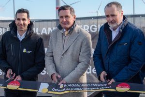 Drei Männer stehen vor einem Banner und schneiden ein Band. Der Mann in der Mitte trägt einen grauen Mantel. Der Mann auf der rechten Seite trägt eine blaue Jacke. Der Mann auf der linken Seite trägt einen schwarzen Mantel. Das Banner steht für 'Burgenland Energie'.