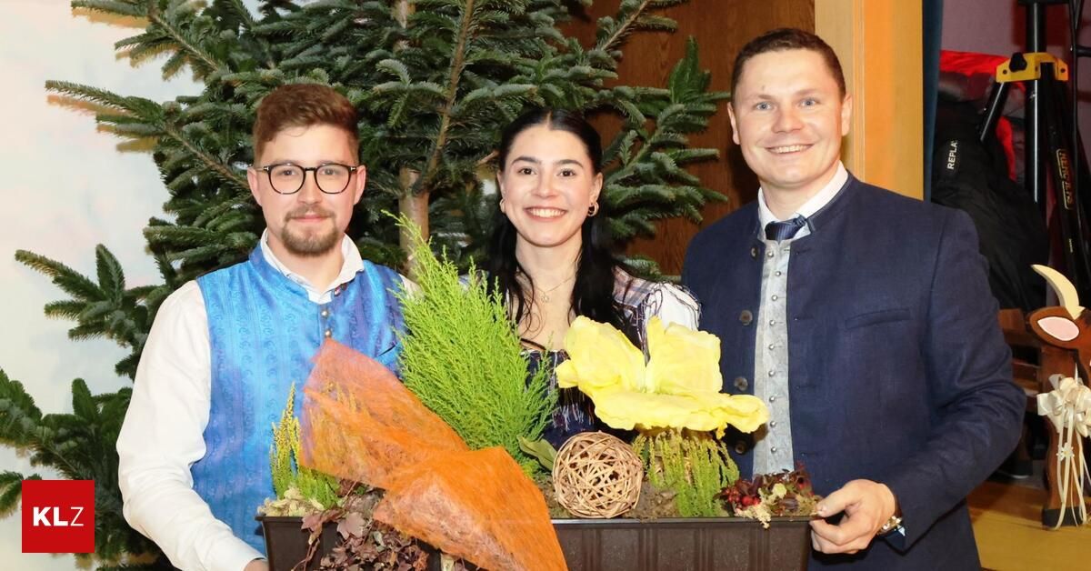 Drei Menschen stehen lächelnd zusammen für ein Foto. Eine Frau hält einen Blumenstrauß vor ihnen.