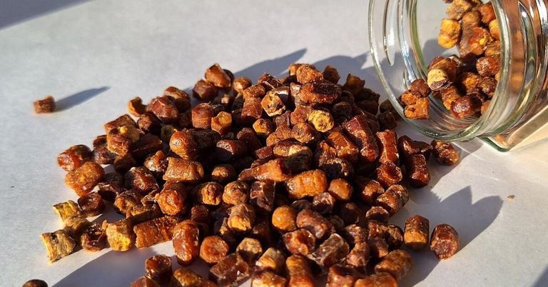 A pile of dried, sliced ginger root on a white surface, with some pieces in a glass jar.