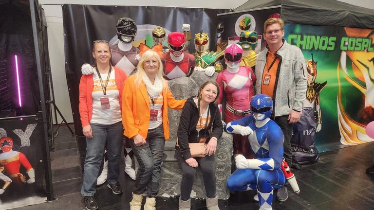 Eine Gruppe von Menschen posiert für ein Foto mit Power Rangers-Kostümen und einem Mann mit Brille.