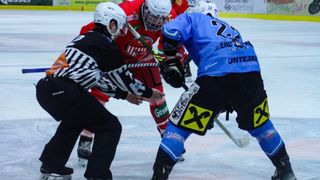 Four ice hockey players in protective gear on an ice rink, one player is being held by a referee while another holds a hockey stick.