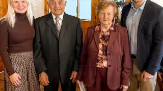 Four people are standing next to each other, smiling for a photo in a room with wooden walls.