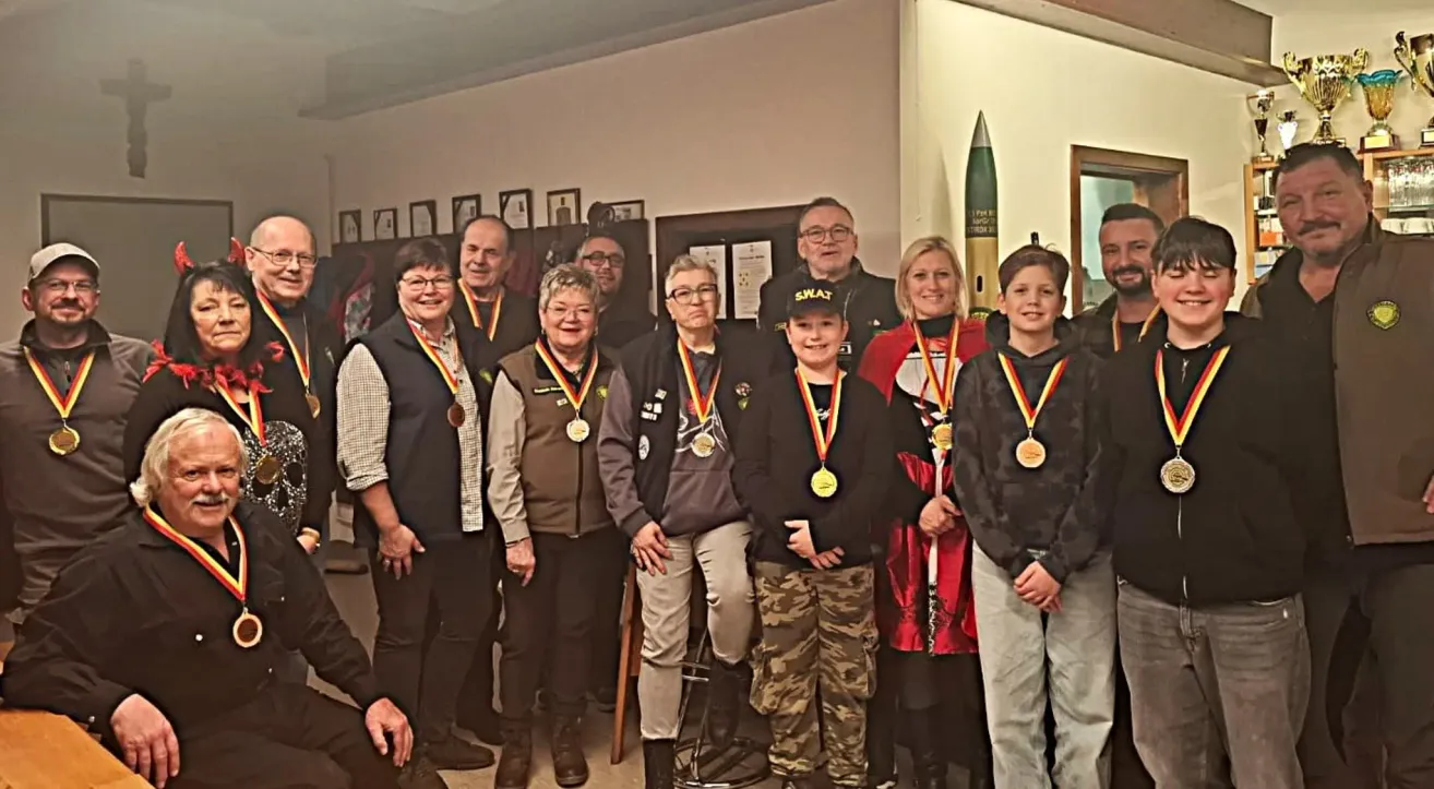 A group of people wearing medals and jackets are posing for a photo in front of a wall with frames and a missile.