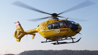 A yellow helicopter marked with a red cross and the letters 'OAMTC' is flying in the sky.