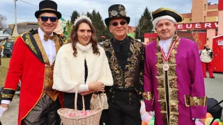 Four people in elaborate costumes, two men and a woman, pose for a photo at a carnival, holding a basket of candies.