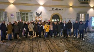 A group of people pose for a photo in front of a building with the sign Rathaus and 400 above an eagle icon.