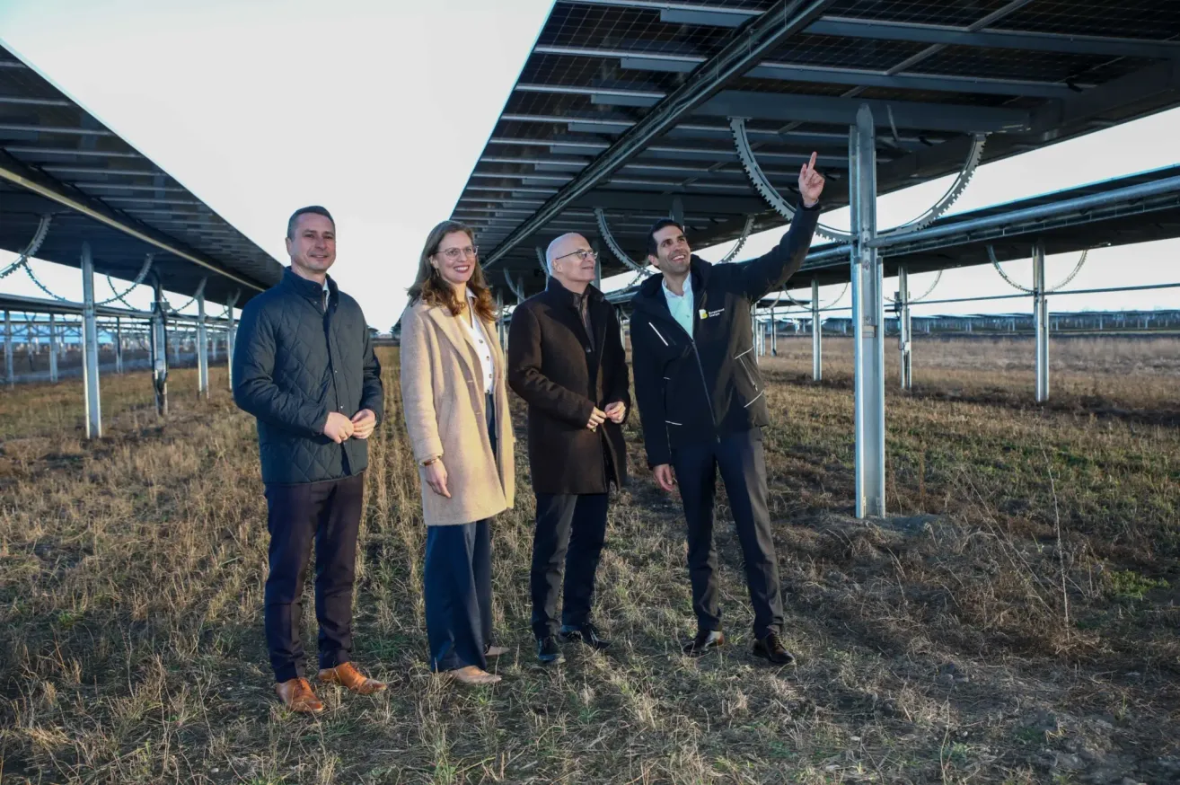 Four individuals are standing in a field with solar panels in the background, smiling and posing for a photograph.
