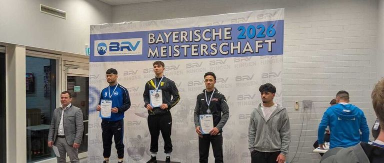 Athletes stand on a podium with medals around their necks, likely for a competition, with a banner behind them that reads 'Bayerische Meisterschaft 2026'.