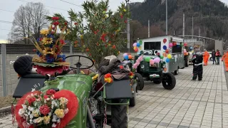 Decorated tractors are parked on a cobblestone street with people in orange safety suits. Mountains and trees are in the background.