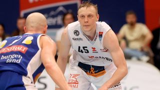 A basketball player in a white jersey with the number 45 is playing in an indoor court. Another player is in the background.