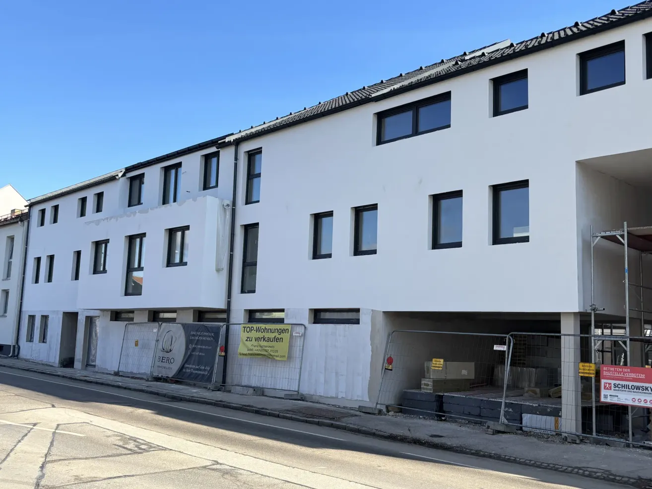 A new white apartment building under construction. It has glass windows, a garage, and a banner indicating it's for sale.