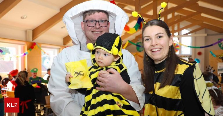 Ein Mann in einem Imkeranzug hält ein Baby in einem Bienenkostüm, während eine Frau in einem ähnlichen Kostüm lächelt.