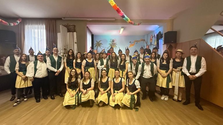 Eine Gruppe von Menschen in traditionellen Kostümen posiert für ein Foto in einem dekorierten Raum, einige stehend und andere sitzend, mit farbenfrohen Dekorationen, die von der Decke hängen.