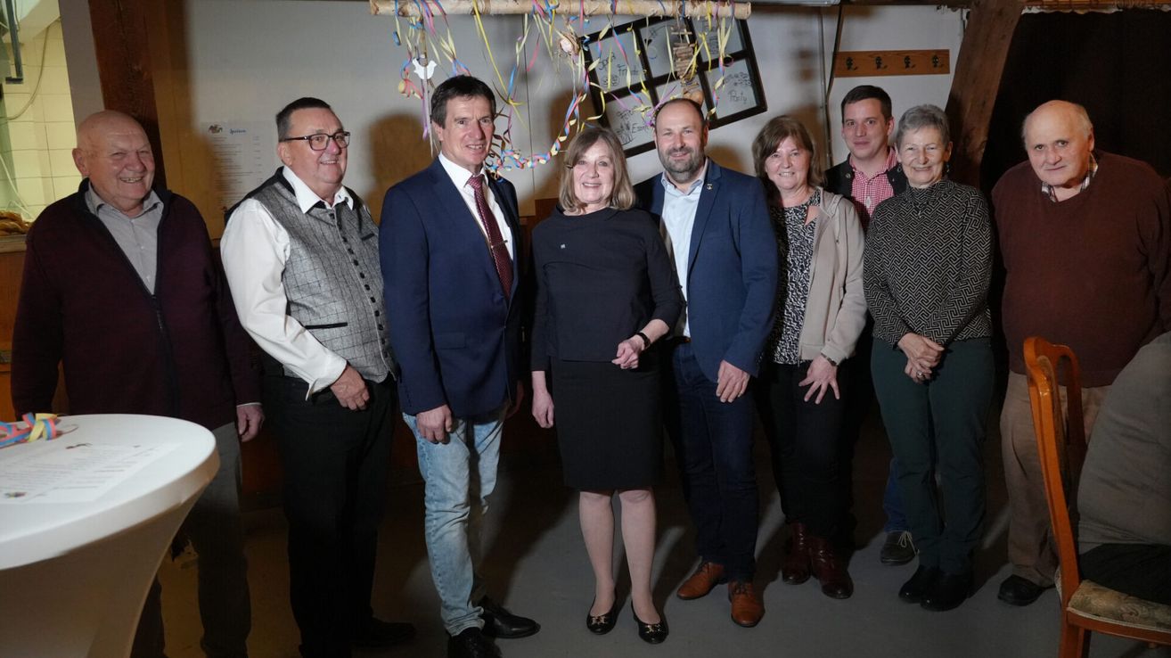 Seven people in formal attire, possibly a family, are posing for a photo in a room with colorful streamers.