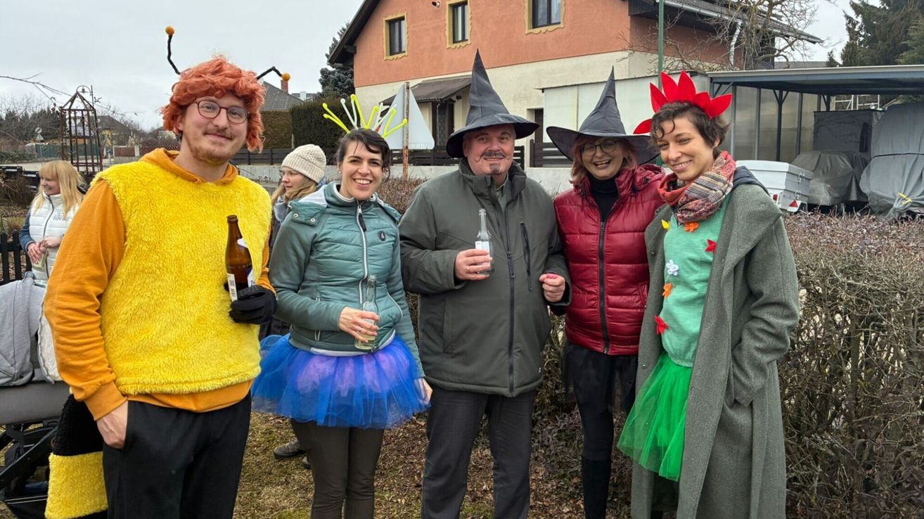 Fünf Menschen in Kostümen posieren für ein Foto vor einem Gebäude. Einer trägt einen Hexenhut, ein anderer ein Tutu und drei halten Flaschen.