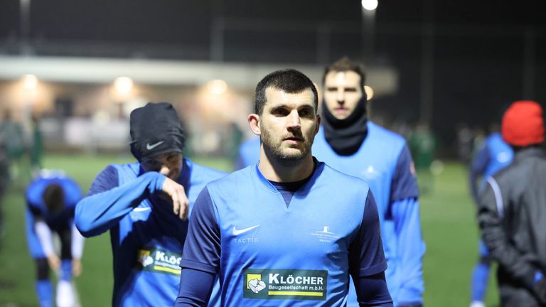 Three men in blue uniforms are on a field at night. The man in front has a serious expression.