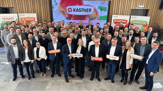 Eine Gruppe von Personen posiert für ein Foto vor einem Kastner-Banner. Viele von ihnen halten Kastner-Schilder in der Hand.