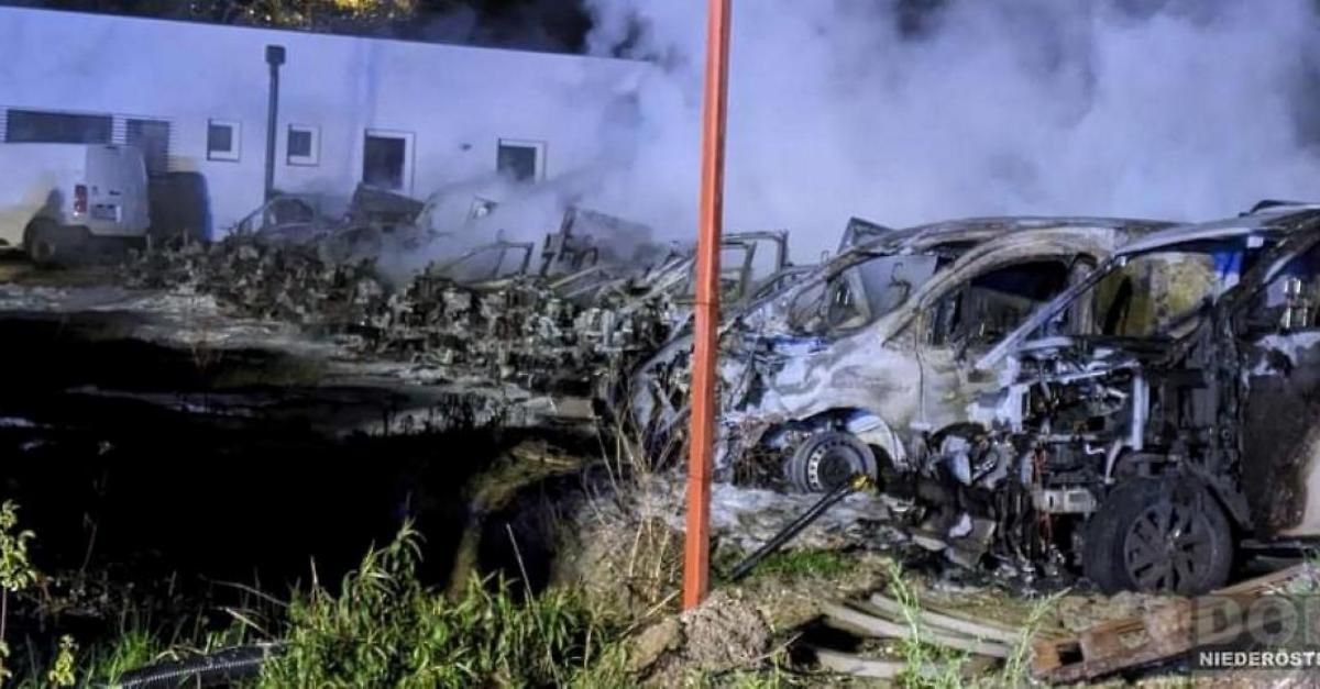 Die Folgen eines schweren Unfalls mit mehreren Fahrzeugen, bei dem ein Fahrzeug völlig zerstört und andere beschädigt sind und in der Nähe eines Gebäudes Rauch ausströmen.