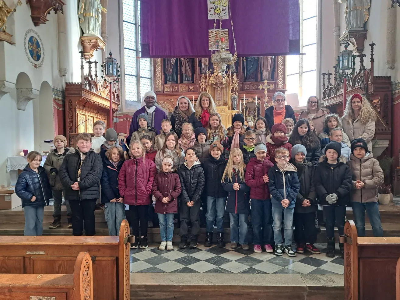 Eine Gruppe von Kindern und Erwachsenen steht in einer Kirche und posiert für ein Gruppenfoto vor dem Altar.