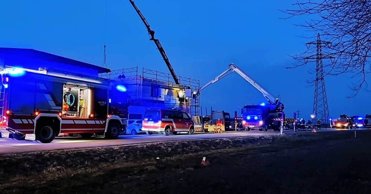 Einsatzfahrzeuge, darunter Feuerwehrwagen, sind auf der Straße geparkt. Ein Feuerwehrwagen hat einen Kran angebracht. Eine Person steht neben dem Feuerwehrwagen.