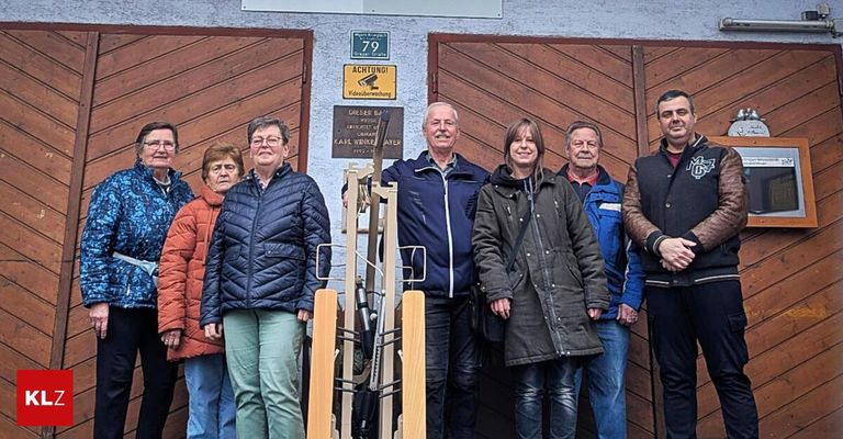 Eine Gruppe von Menschen in Winterkleidung posiert für ein Foto vor einer Holztür mit Schildern und einem gelben Warnschild.