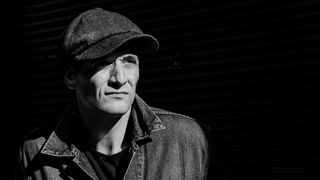 Schwarz-Weiß-Porträt eines Mannes mit Schirmmütze und Jeansjacke, der leicht lächelt.